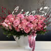 Pink roses and ranunculus in a white textured vase with a pink ribbon