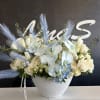 White floral arrangement with pale blue orchids in a textured white vase