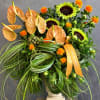 Tropical arrangement with orange anthuriums, sunflowers, and orange ribbon in a vase