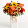 Bouquet of sunflowers, roses, and mums in a white vase with a ribbon