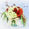 Low glass vase arrangement with white hydrangeas, red roses, and orange gerbera daisies tied with a cream bow.