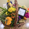 Autumn gift basket with yellow and orange flowering plants, a pumpkin, candle, and fall decorations