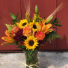 Bouquet of sunflowers, orange lilies, and roses in a glass vase