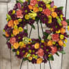 Floral wreath on a stand with orange roses, purple daisies, and pink carnations