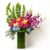 Tall arrangement of pink roses, orchids, and blue hydrangeas in a green-lined glass cylinder vase