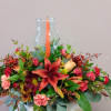 Mixed floral arrangement in a clear glass vase with an orange candle