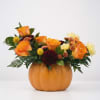 Orange roses and mixed flowers arranged in a pumpkin-shaped vase
