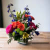 Colorful mixed bouquet in a square vase with roses and lilies