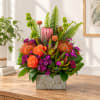 Tropical floral arrangement with orange roses in a patterned rectangular vase