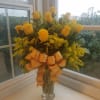 Yellow roses in a clear glass vase with a gold ribbon