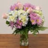 Pink daisies and roses arranged with pale hydrangeas in a glass vase