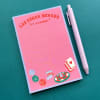 Pink notepad with Las Vegas graphics and a pen on a teal surface