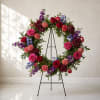 Floral wreath of roses, carnations, and purple blooms on a black stand