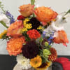 Mixed bouquet in a pumpkin-shaped vase with orange, white, yellow, and dark blooms