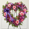 Heart-shaped floral wreath with pink and purple roses on a stand