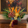 Tropical flower arrangement in a burgundy vase with orange and purple blooms