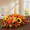 All-around centerpiece arrangement with autumn-colored roses, sunflowers, red daisy poms, orange Asiatic