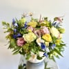 Mixed bouquet of pastel roses, blue flowers, and pink blooms in a vase