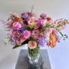 Mixed pink, peach, purple, and orange flowers in a clear glass vase
