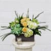 Arrangement of yellow roses, hydrangeas, orchids, and succulents in a rectangular container with a candle