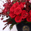 Red roses arranged in a black vase with dark foliage