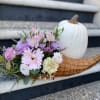 Pastel flower arrangement in a wicker basket beside a white pumpkin