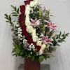 Tall arrangement of red and white roses with pink lilies in a wooden vase