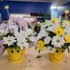 Two daisy arrangements in yellow smiley-face pots, one with pink and white blooms and one with white and yellow blooms.