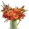 Orange and red flower arrangement in a green ceramic pitcher