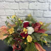 Festive floral arrangement with red roses, white carnations, and lilies in a low design
