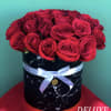 Red roses arranged in a black round box with a white ribbon