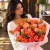 Woman holding a bouquet of coral roses wrapped in pink paper