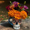 Bright orange and purple flowers arranged in a skull-shaped mug.