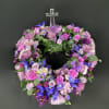 Circular wreath of purple and pink flowers with a clear cross topper