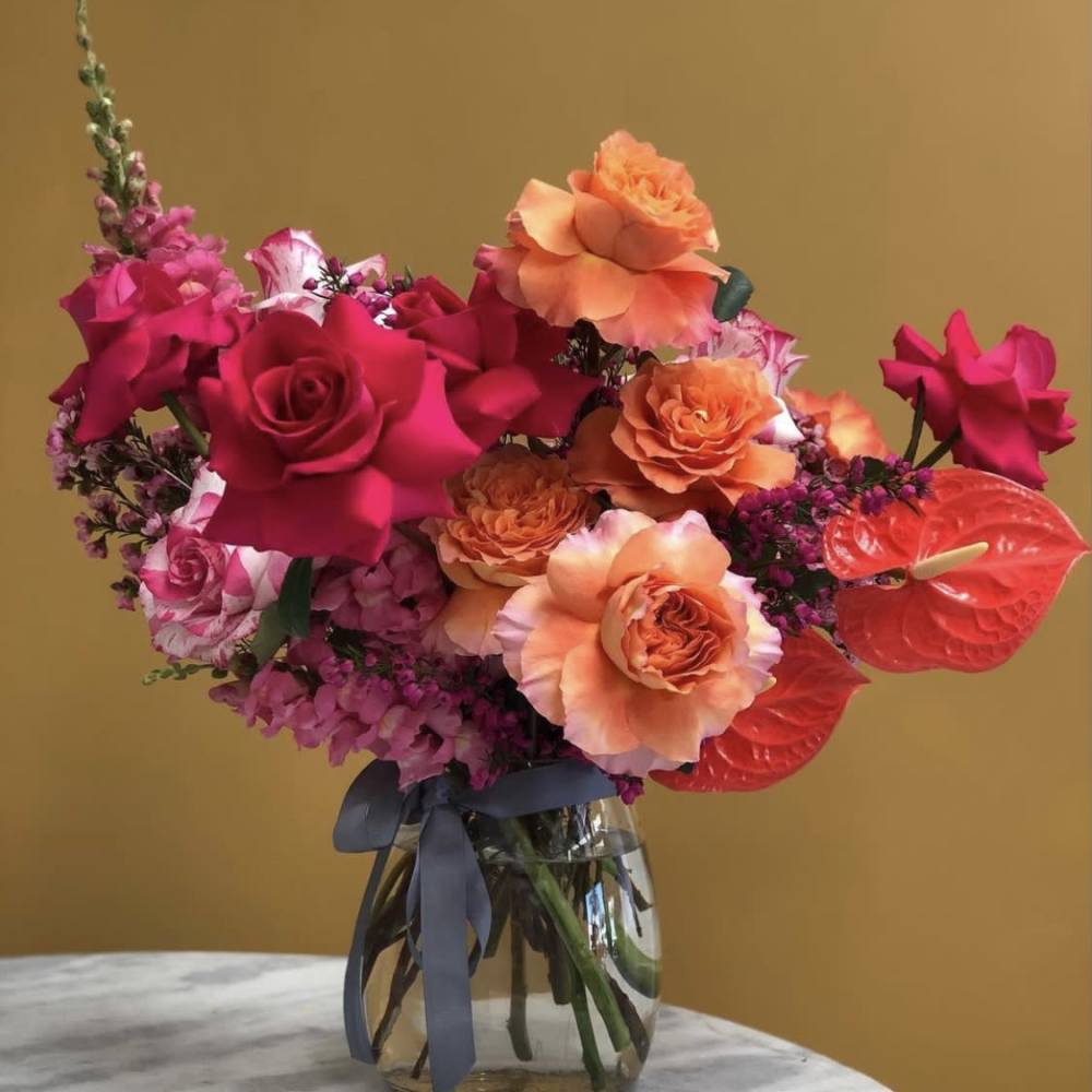Bright pink and orange rose bouquet in a glass vase with a ribbon