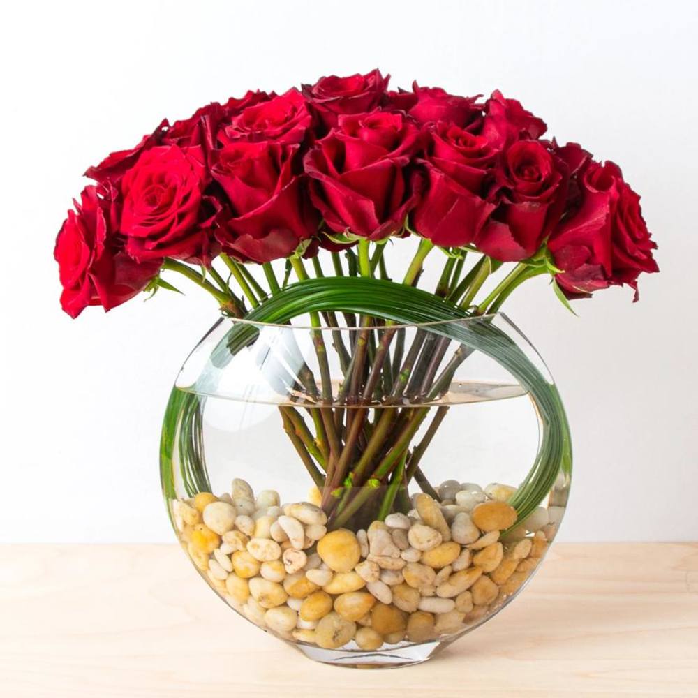 Red roses arranged in a round glass vase with pebbles