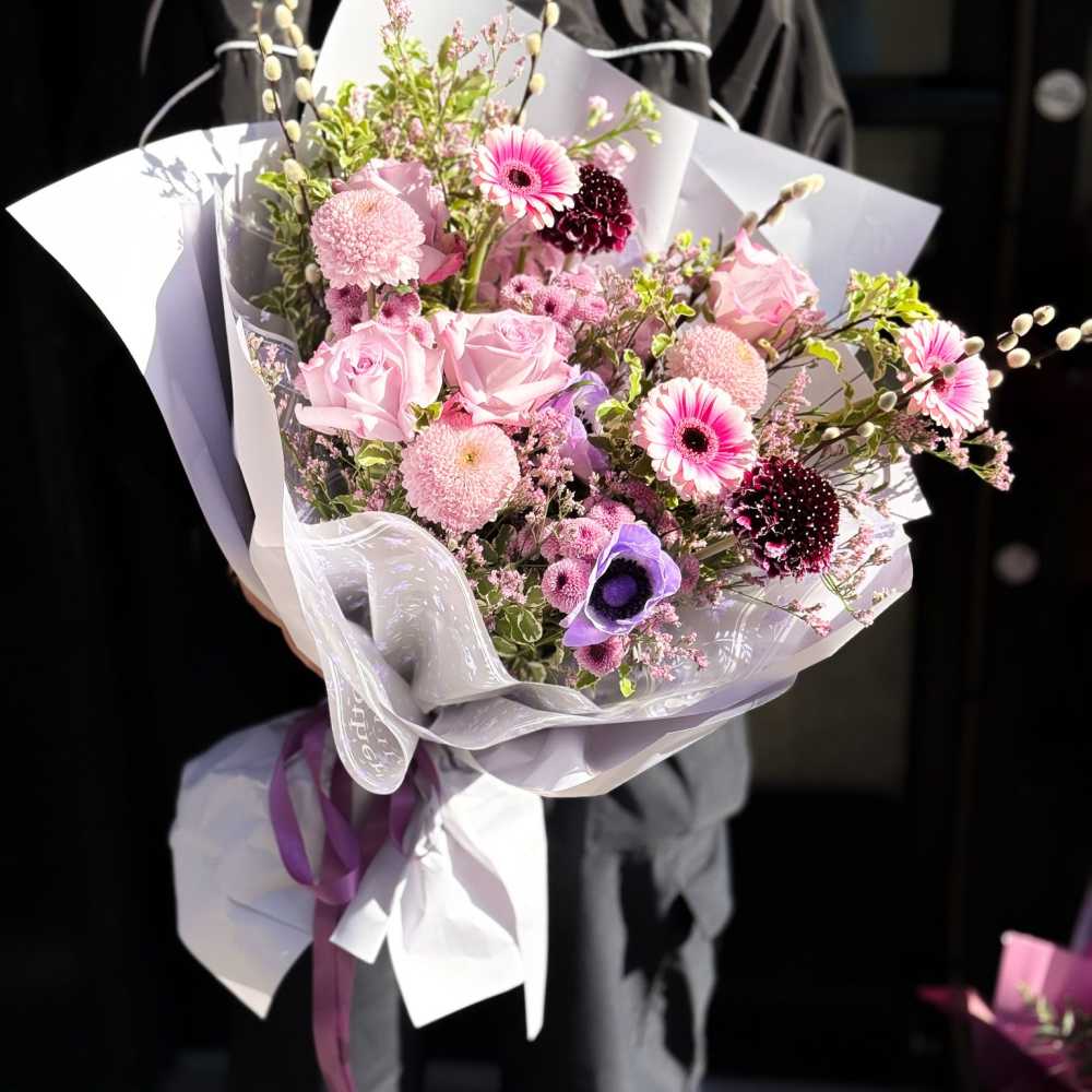 Pink and purple mixed bouquet wrapped in white paper with ribbon