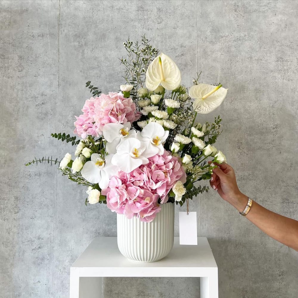 Pink hydrangeas and white orchids arranged in a white vase