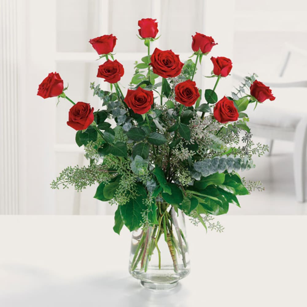 Red roses arranged in a clear glass vase with greenery