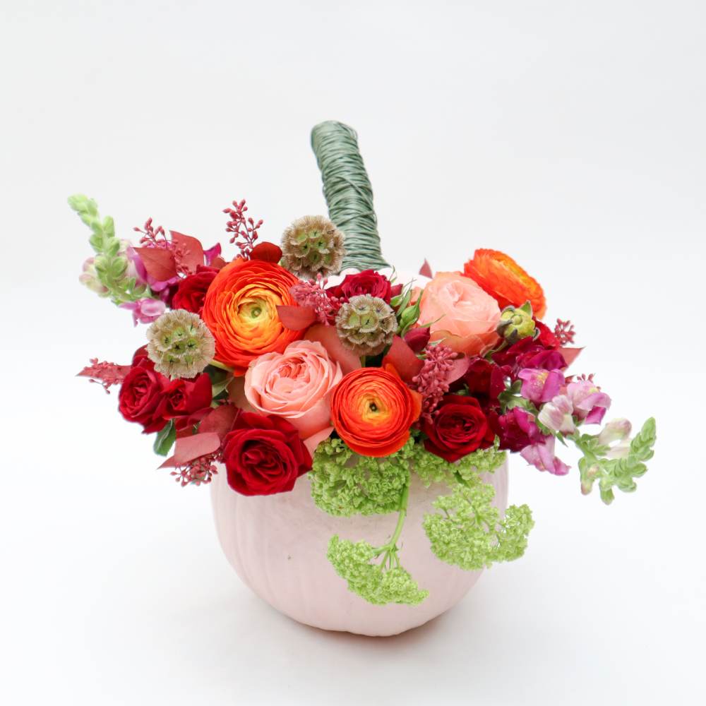 Mixed bouquet of red, pink, and orange flowers in a pale pink vase