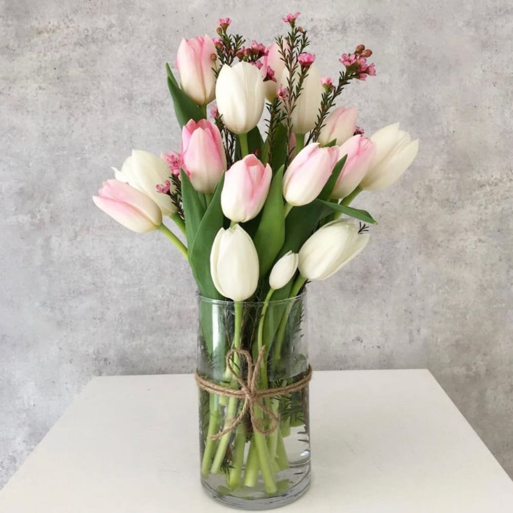 Pink and white tulips in a clear glass vase tied with twine