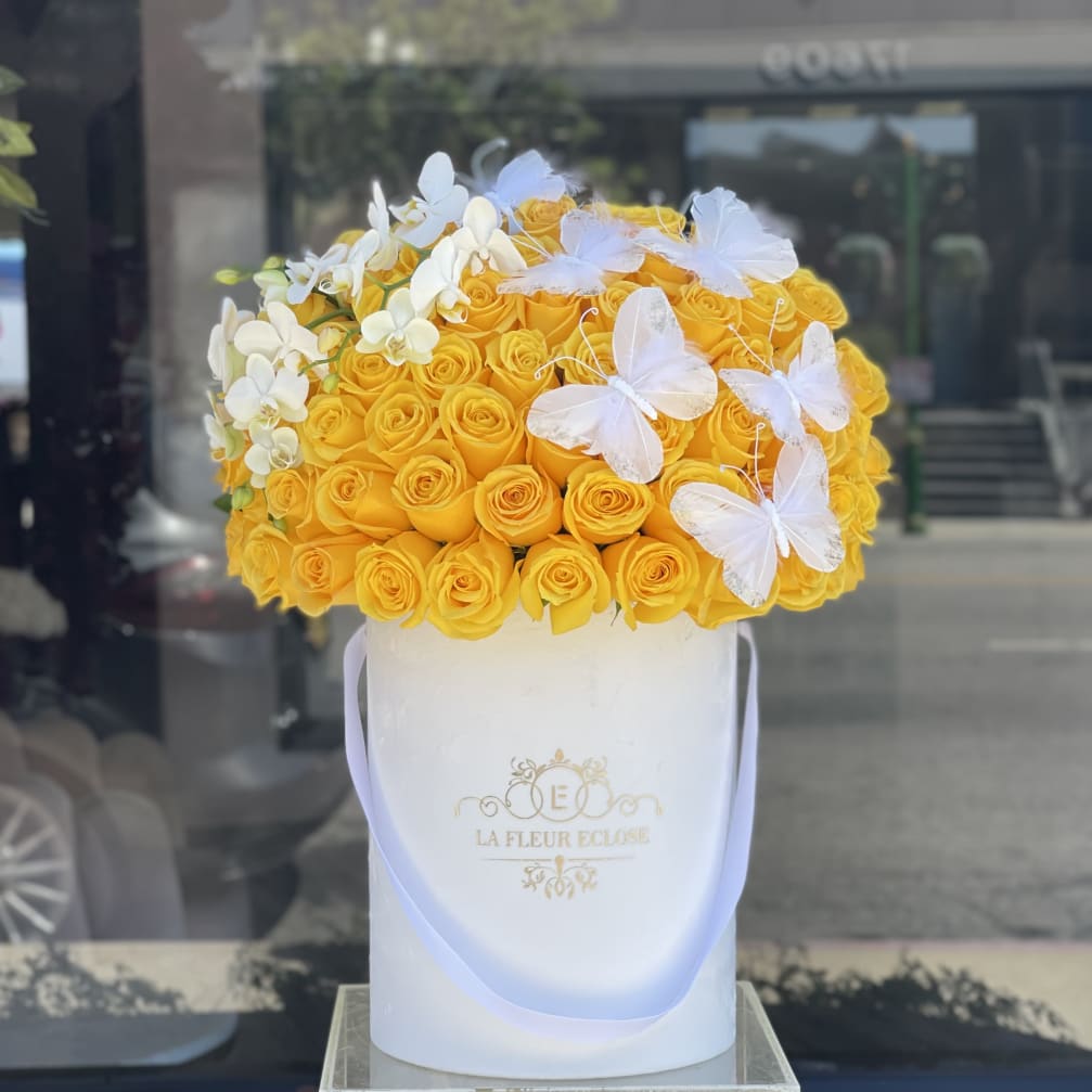 Yellow roses in a white hatbox with white orchids and butterfly decorations