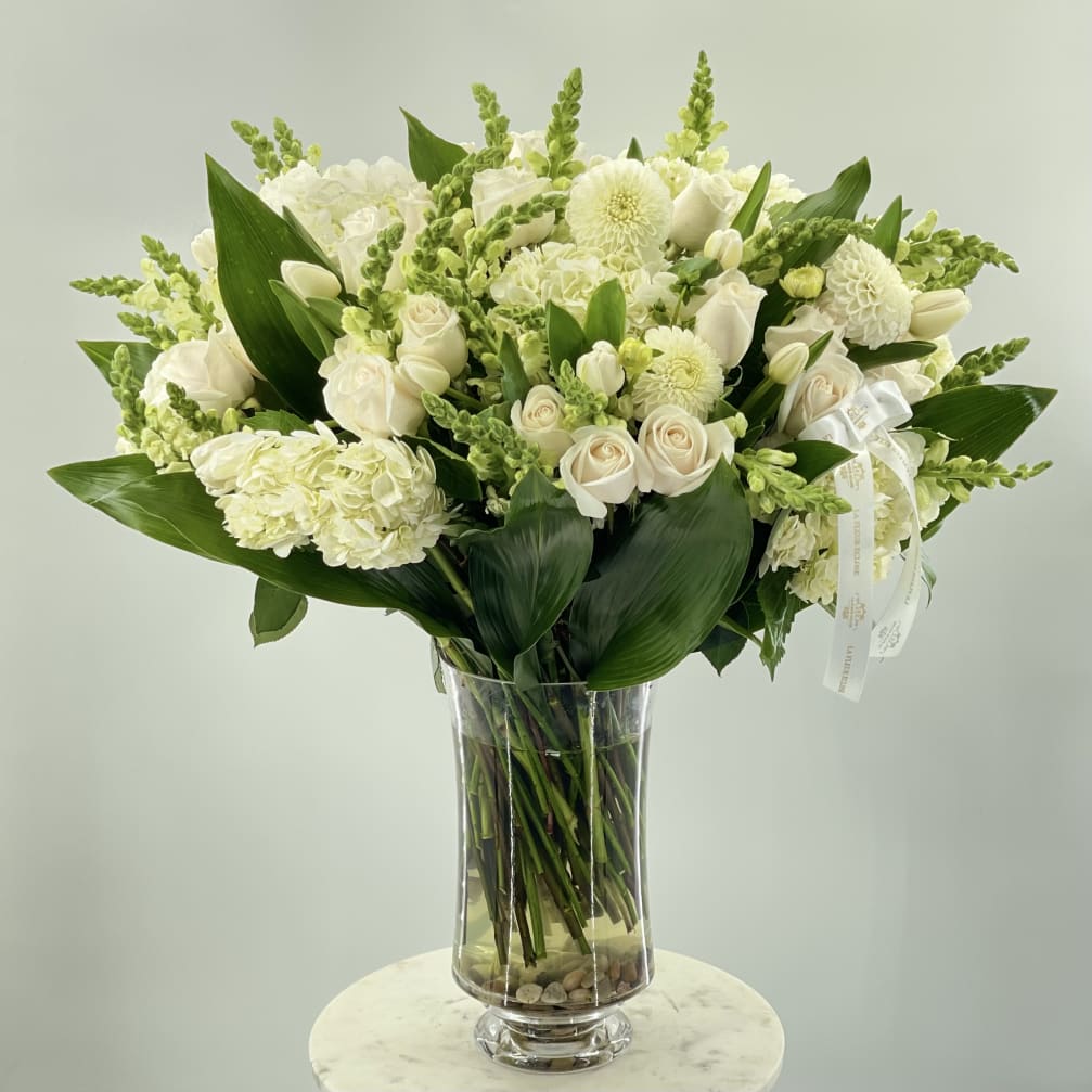 White floral arrangement in a clear glass vase with broad green leaves