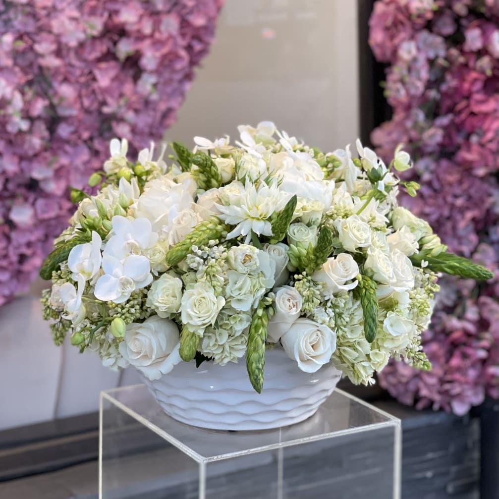 White floral arrangement in a white bowl vase with green accents