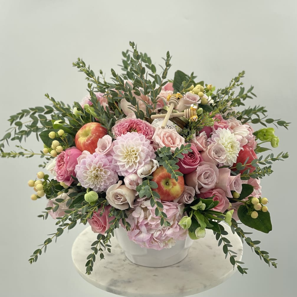 Pink and white flower arrangement in a white vase with apples