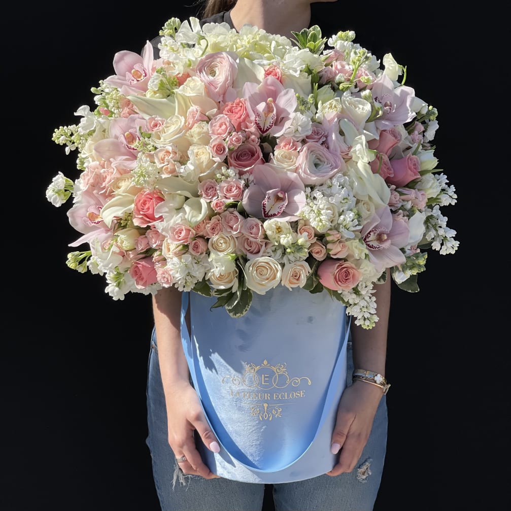 Large pastel bouquet of roses, orchids, and white blooms in a blue hatbox