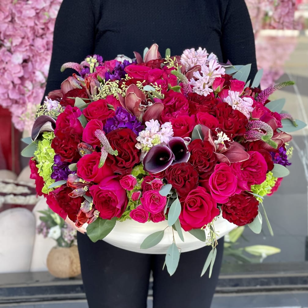 Large bouquet of red and pink roses with purple accents in a white container