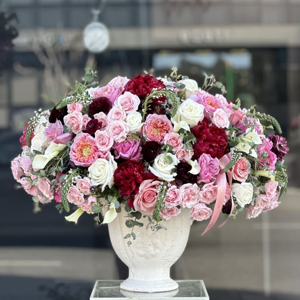 Large pink, white, and red rose arrangement in a white urn vase