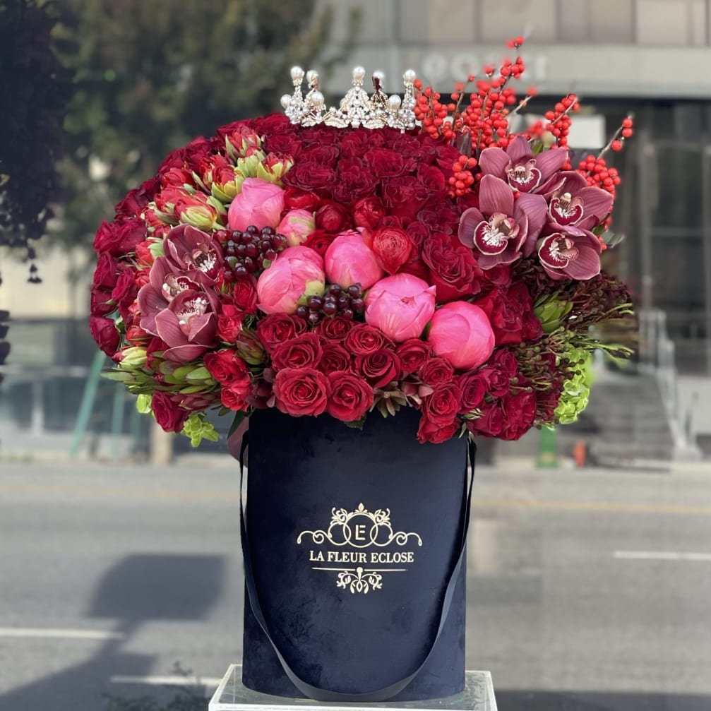 Large red and pink floral arrangement in a black hatbox with a crown topper.