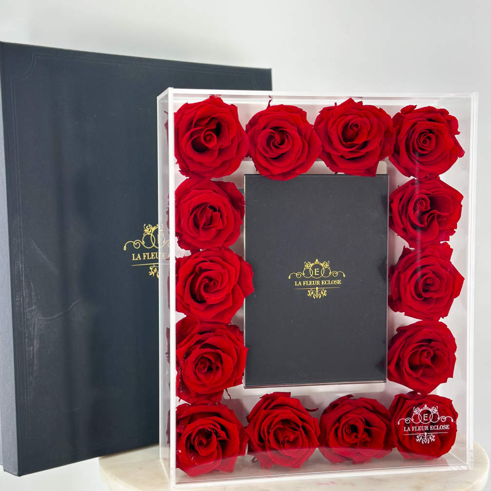 Red roses arranged in a clear box around a black gift box